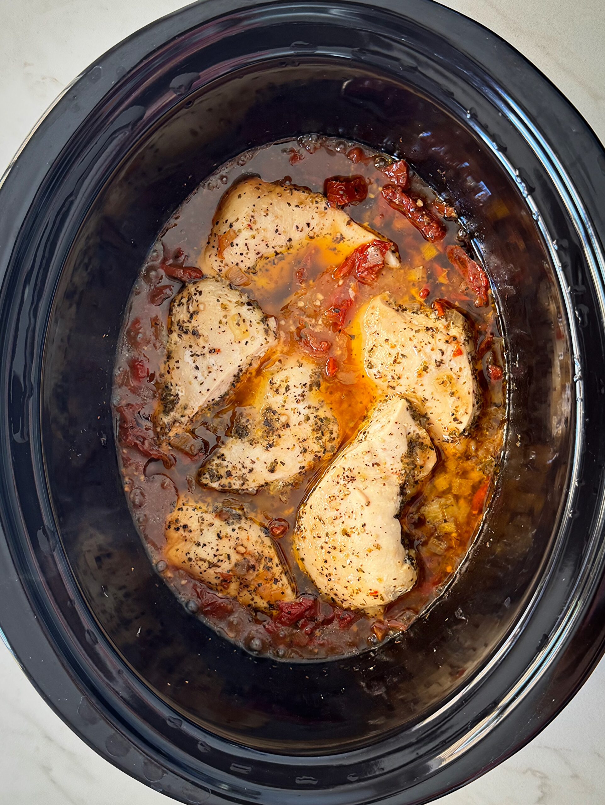 overhead shot of cooked Tuscan chicken in a black slow cooker
