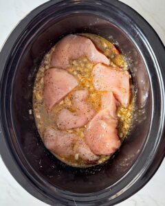 overhead shot of uncooked Tuscan chicken in a black slow cooker