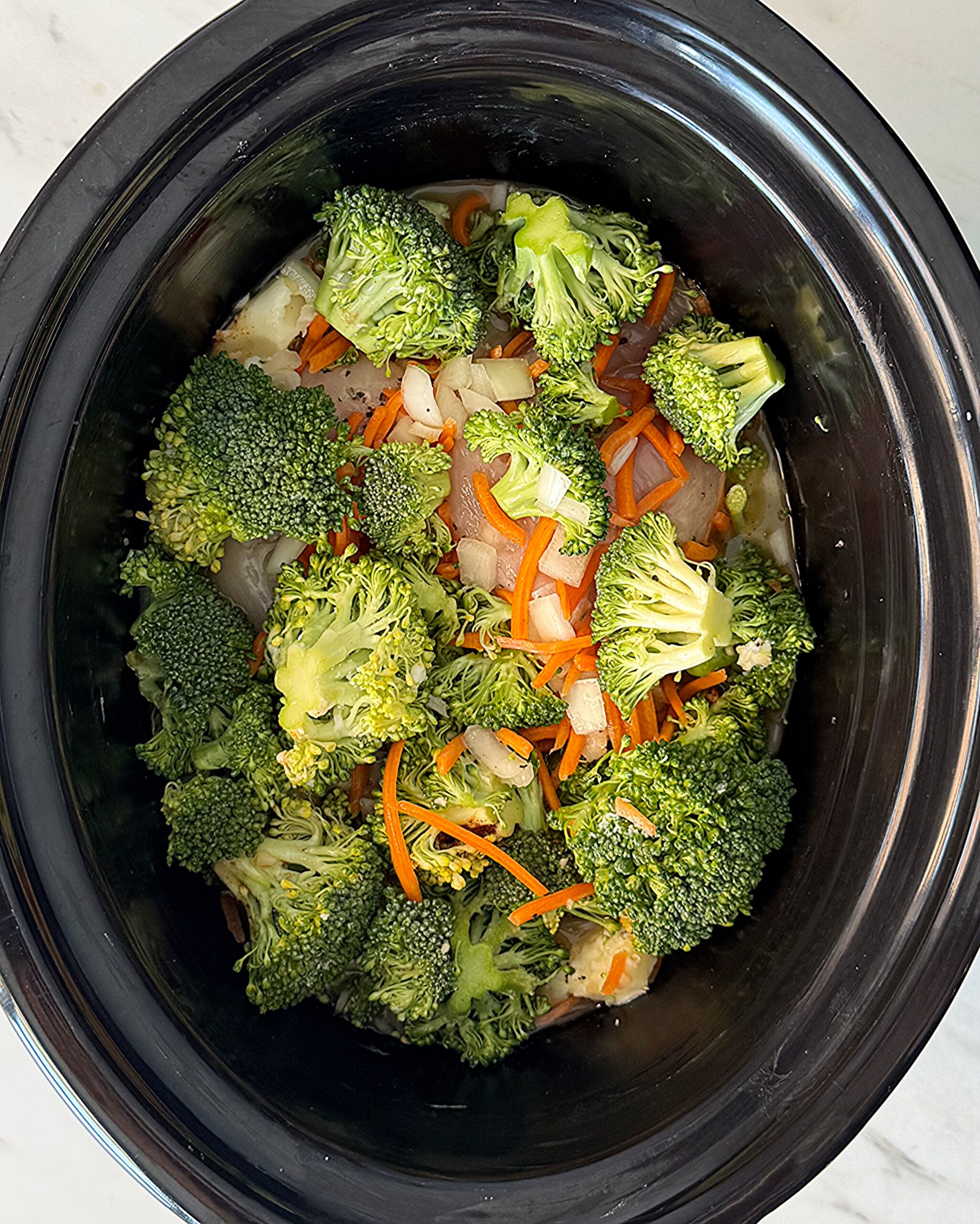 overhead shot of uncooked Chicken Broccoli Cheese Soup in a black slow cooker