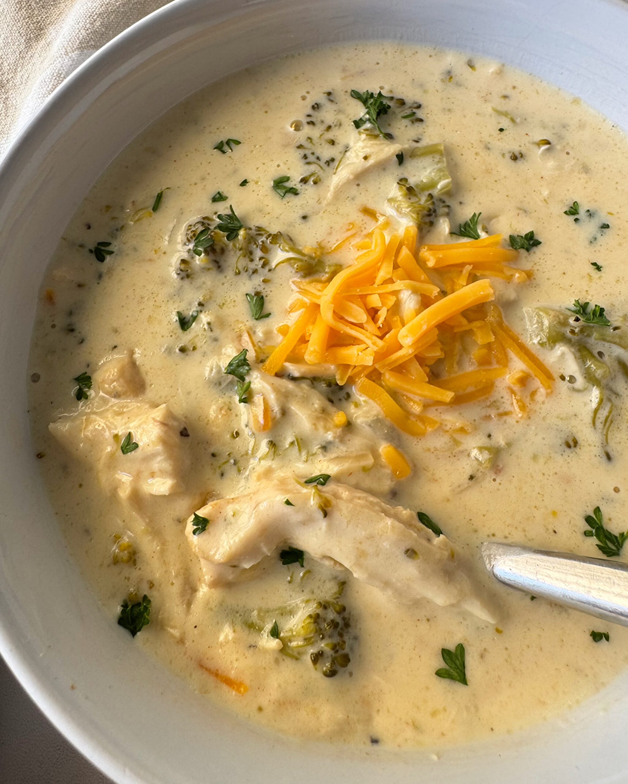 overhead shot of slow cooker Chicken Broccoli Cheese Soup in a white bowl garnished with shredded cheddar cheese