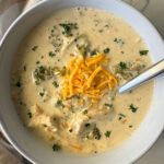 overhead shot of slow cooker Chicken Broccoli Cheese Soup in a white bowl garnished with shredded cheddar cheese