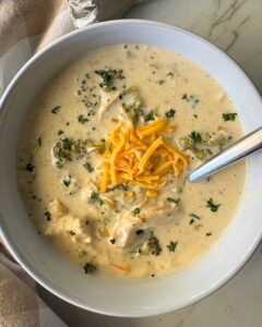 overhead shot of slow cooker Chicken Broccoli Cheese Soup in a white bowl garnished with shredded cheddar cheese