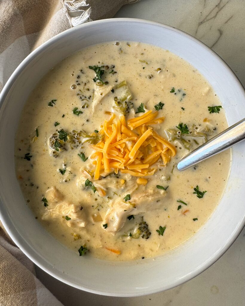 overhead shot of slow cooker Chicken Broccoli Cheese Soup in a white bowl garnished with shredded cheddar cheese