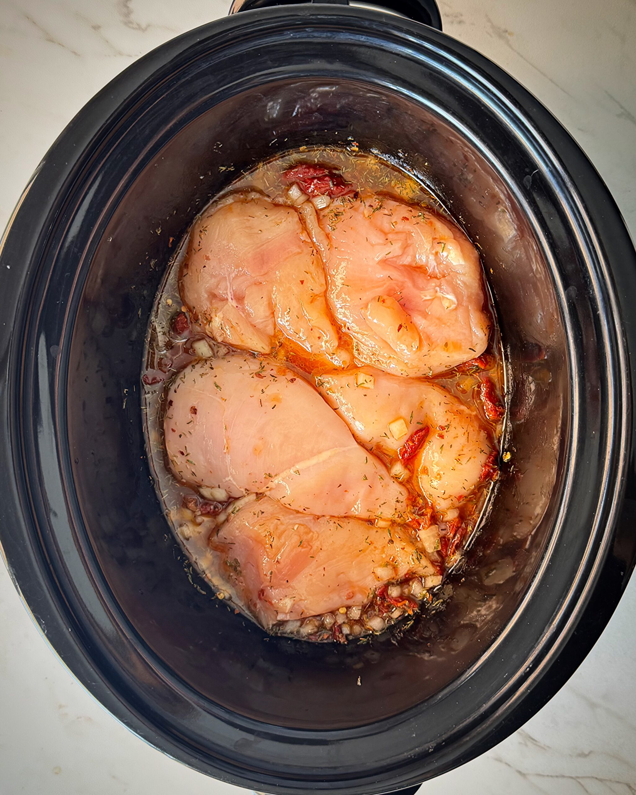 overhead shot of uncooked marry me chicken in a black slow cooker