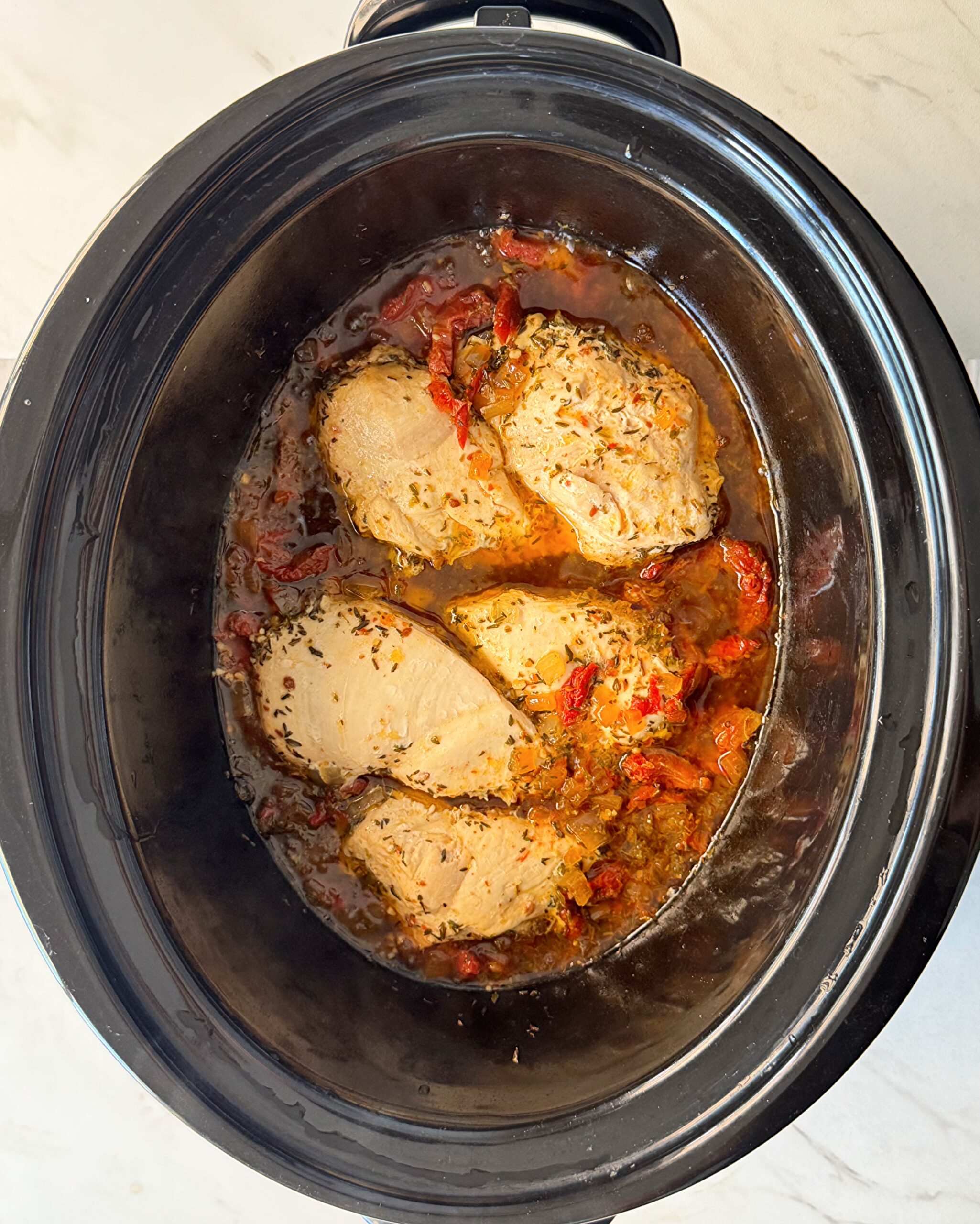 overhead shot of cooked marry me chicken in a black slow cooker