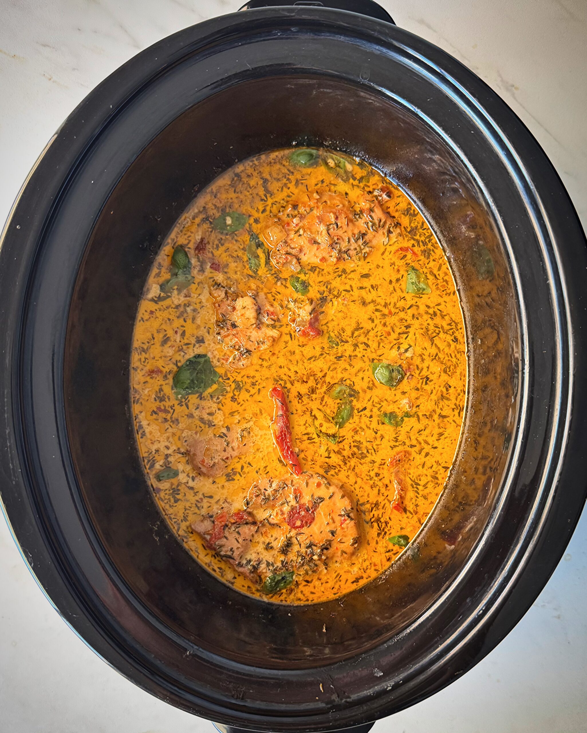overhead shot of cooked marry me chicken in a black slow cooker