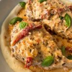 close up shot of cooked marry me chicken served over mashed potatoes in a white bowl