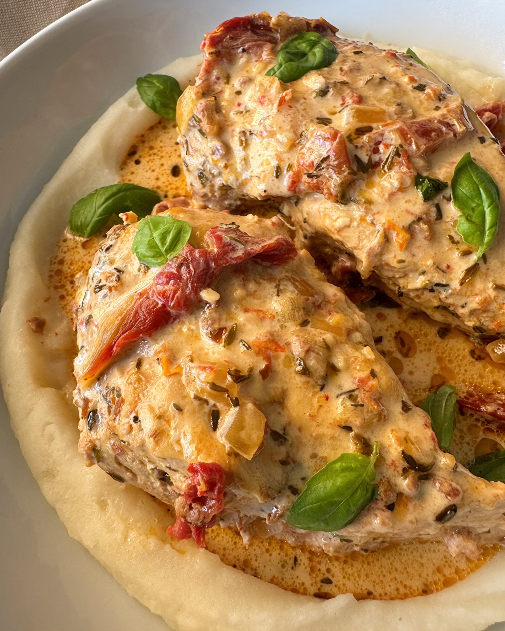 close up shot of cooked marry me chicken served over mashed potatoes in a white bowl
