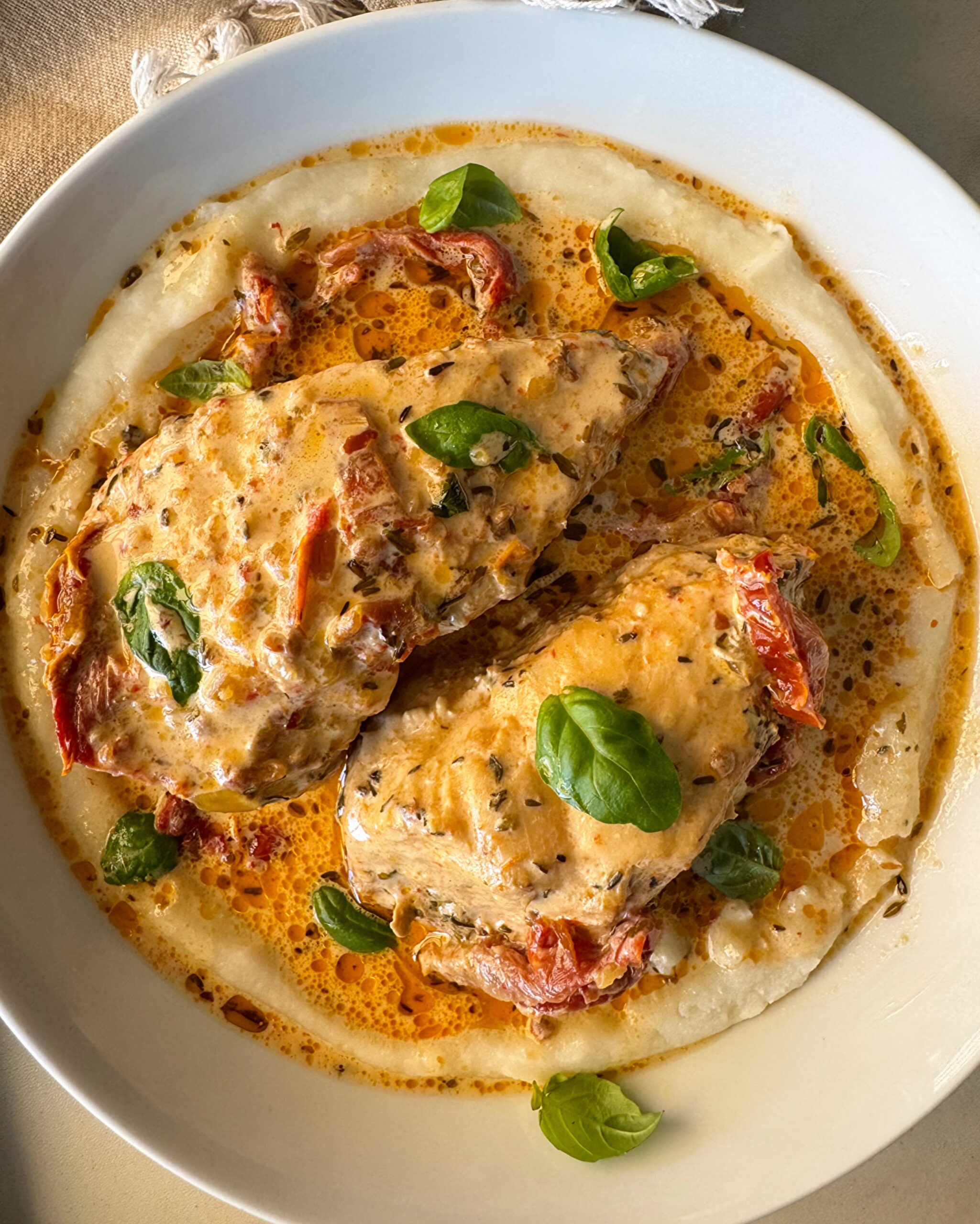 overhead shot of cooked marry me chicken served over mashed potatoes in a white bowl