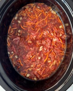 overhead shot of uncooked beef udon soup in a black slow cooker