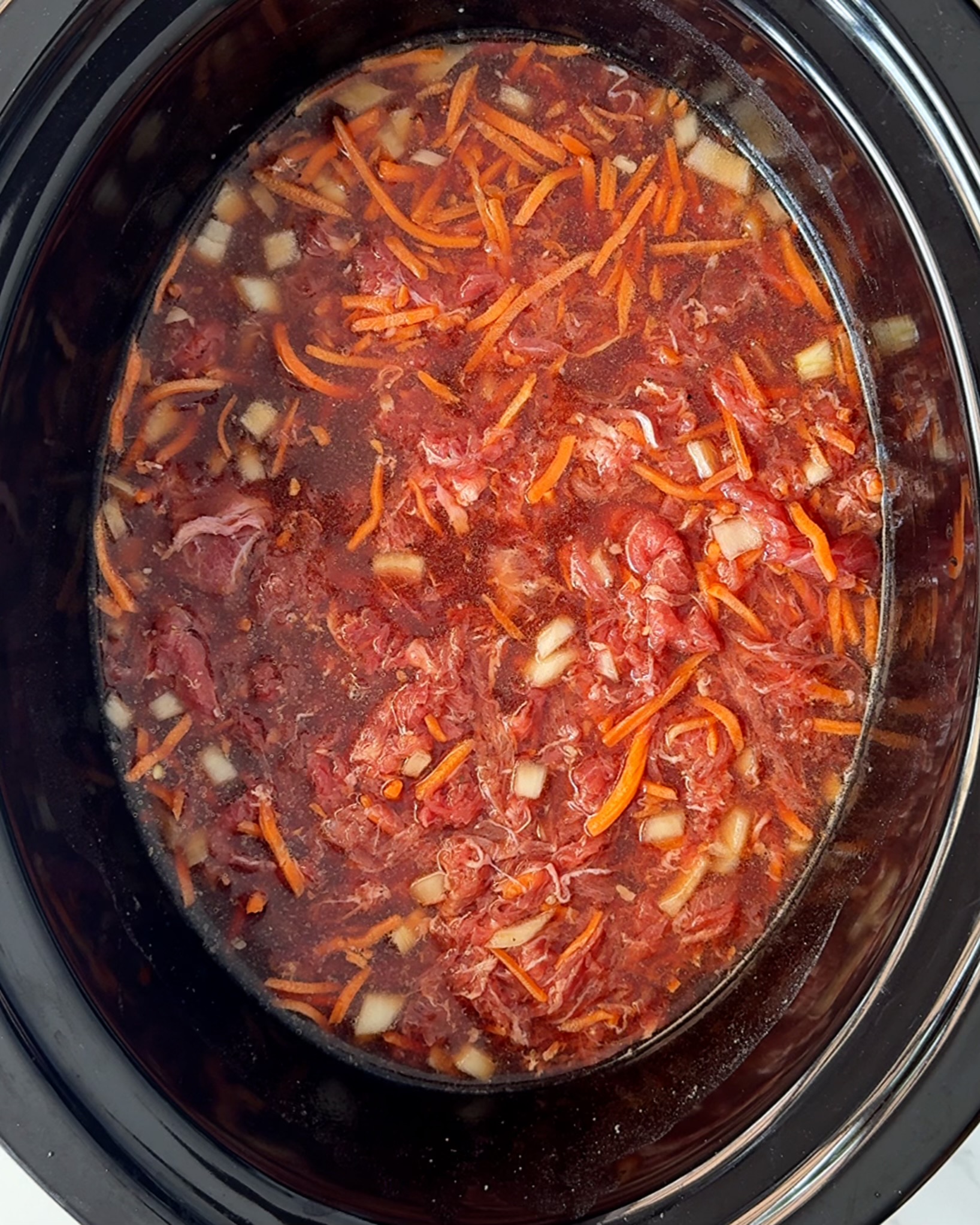 overhead shot of uncooked beef udon soup in a black slow cooker