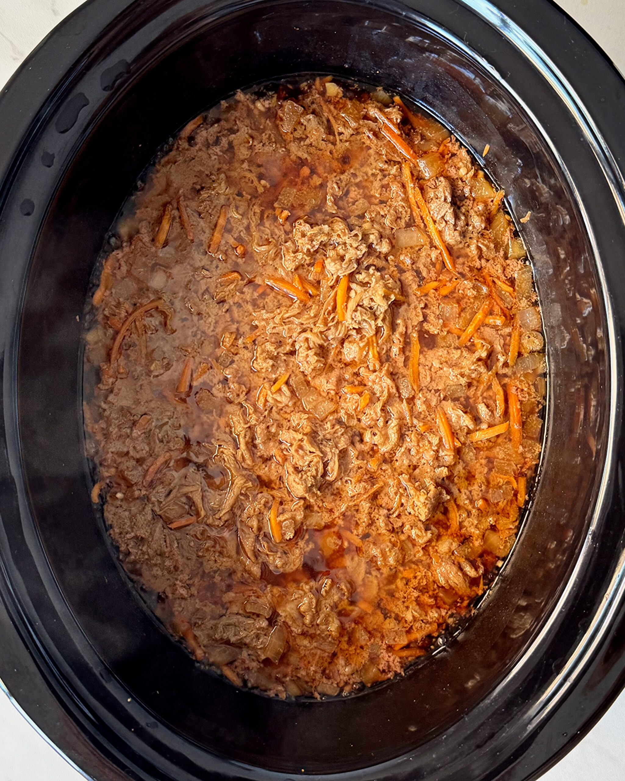 overhead shot of cooked beef udon soup in a black slow cooker