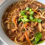 close up shot of beef udon soup in a white bowl garnished with green onion