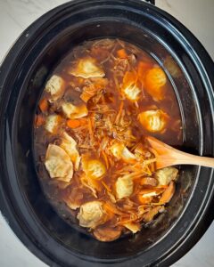 overhead shot of cooked potsticker soup in a black slow cooker with potstickers added
