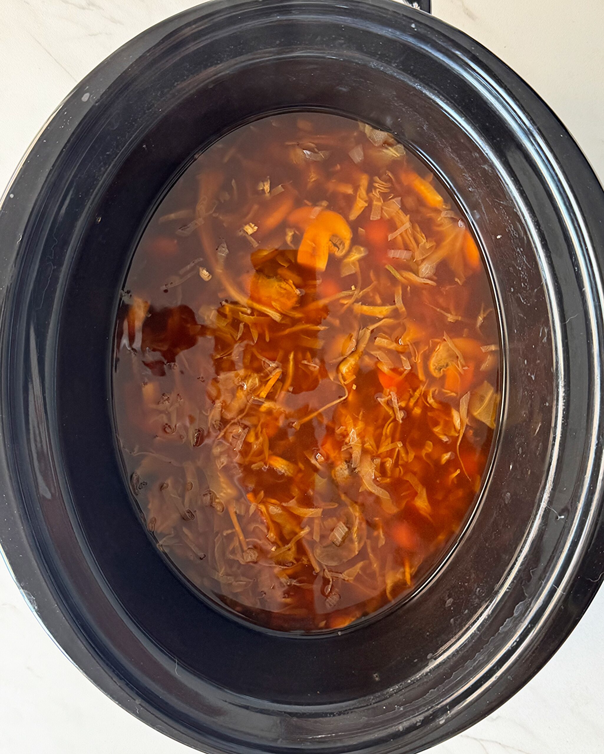overhead shot of cooked potsticker soup in a black slow cooker