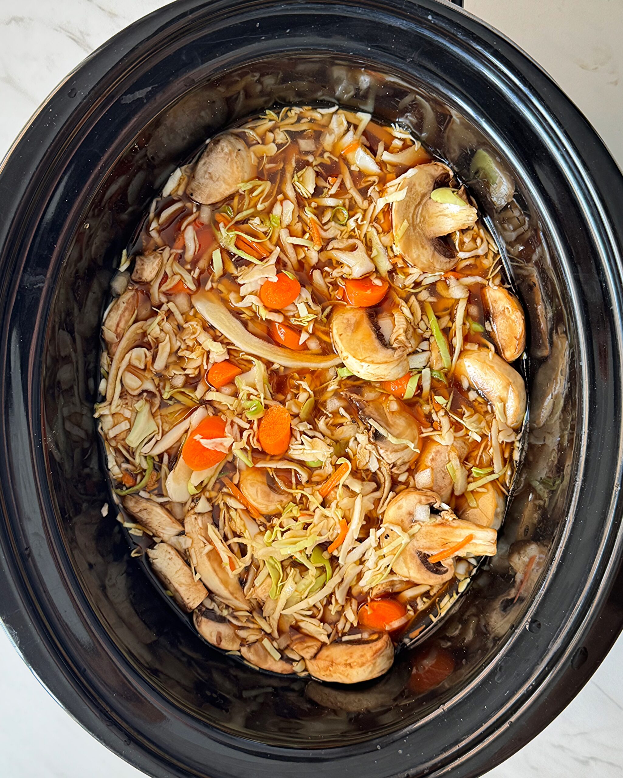 overhead shot of uncooked potsticker soup in a black slow cooker