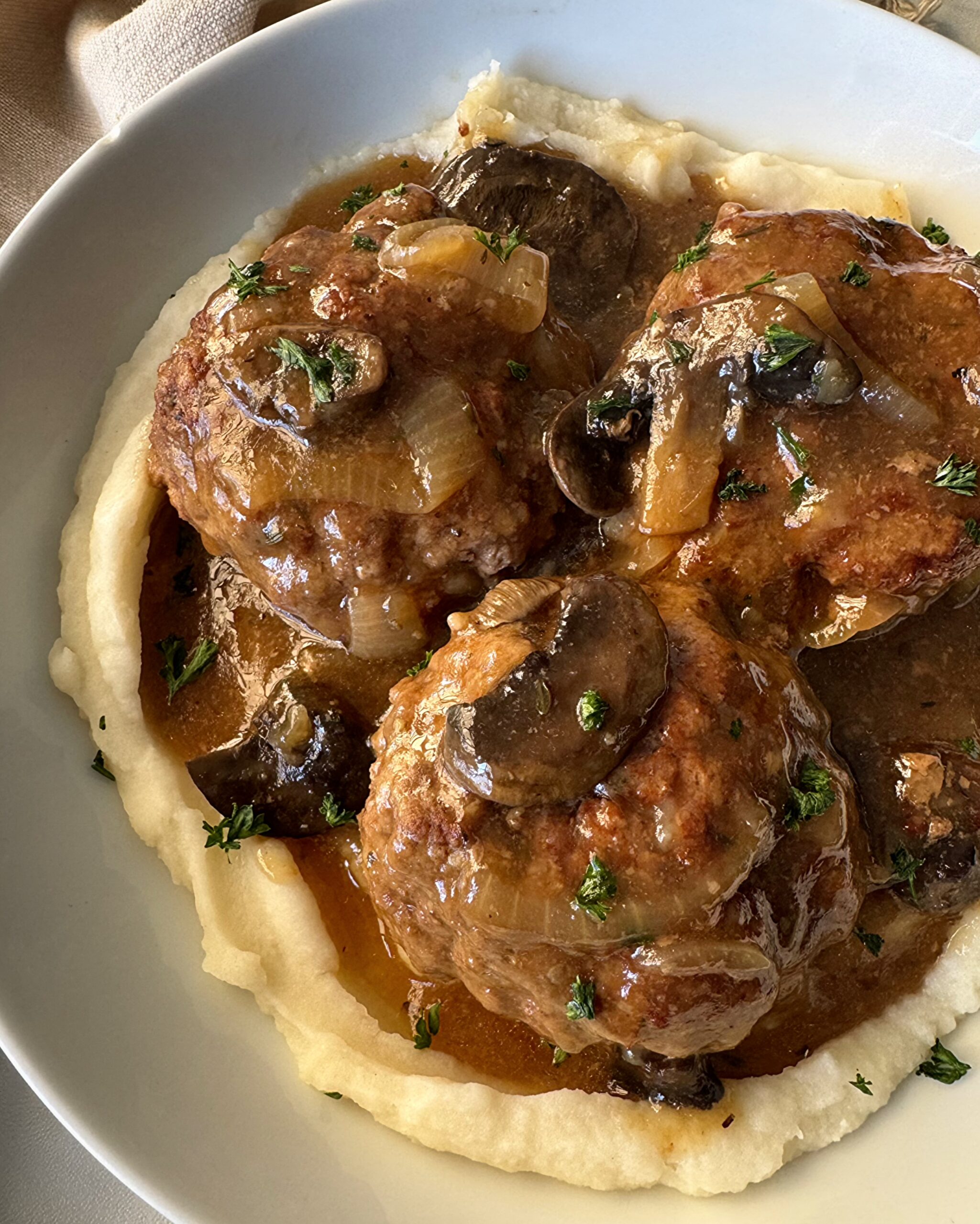 close up shot of Slow Cooker Salisbury Steak on a white plate served over mashed potatoes